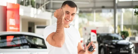 Homem em locadora comemorando segurando a chave de seu carro alugado 