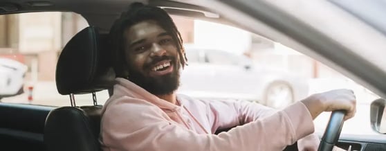 Motorista de aplicativo sorridente segurando o volante dentro do carro