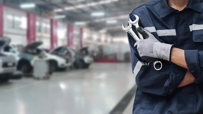 Close em um mecânico vestindo uniforme e segurando ferramentas, com oficina ao fundo