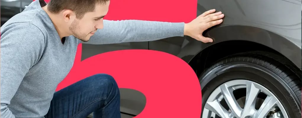 Homem abaixado inspecionando o pneu do carro, 5 principais cuidados