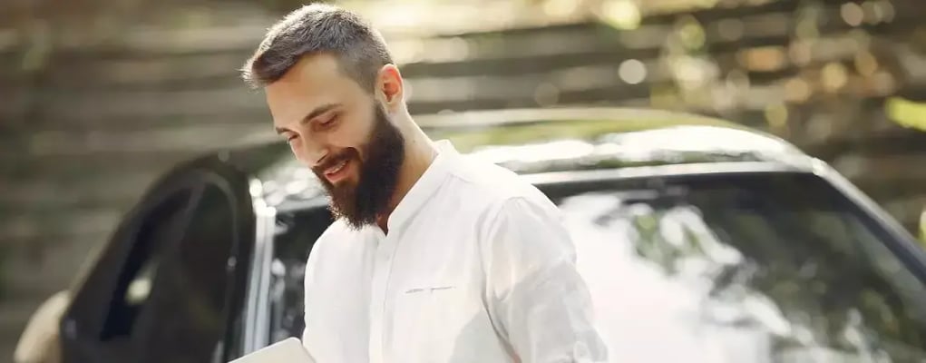 Homem sorrindo enquanto está encostado no carro