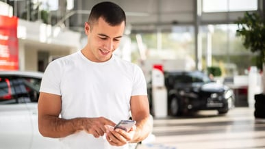 Homem sorrindo e usando celular dentro de uma loja de carros