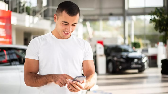 Homem sorrindo e usando celular dentro de uma loja de carros