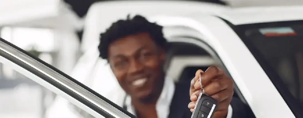 Homem sorrindo ao fundo, enquanto sua mão em primeiro plano segura a chave do carro