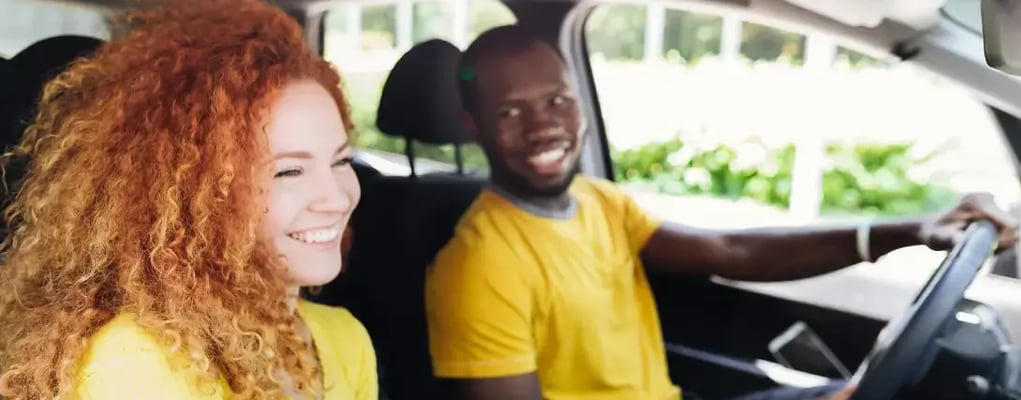 Homem feliz dirigindo o carro olhando para mulher no banco do passageiro