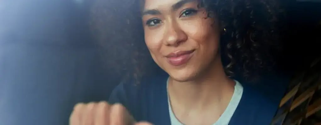 Mulher motorista de aplicativo apoiada no volante sorrindo olhando para fora da janela