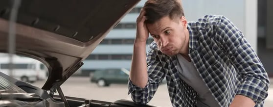 Homem com expressão de preocupação olhando para um carro com o capô aberto