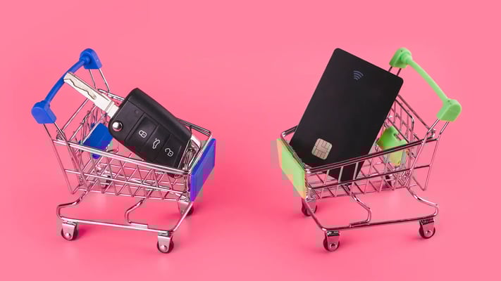 Dois carrinhos de supermercado em miniatura: um com chave de carro e outro com cartão de crédito, sobre fundo rosa