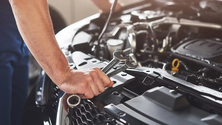 Mecânico segurando ferramentas olhando para o motor de um carro
