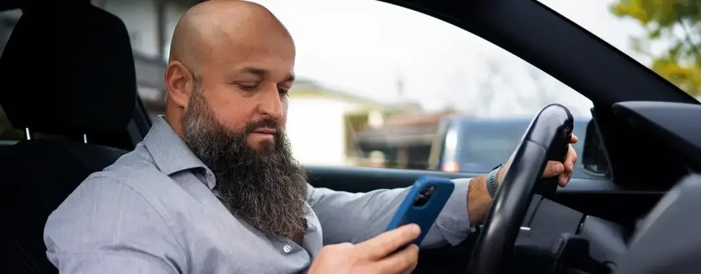 Homem olhando para o celular dentro do carro, motorista de aplicativo