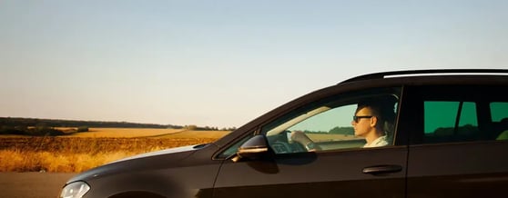 Visão lateral de carro na estrada, sendo dirigido por um motorista com óculos escuros