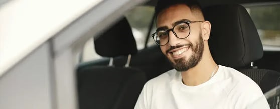 Homem de óculos dentro de carro sorrindo para câmera