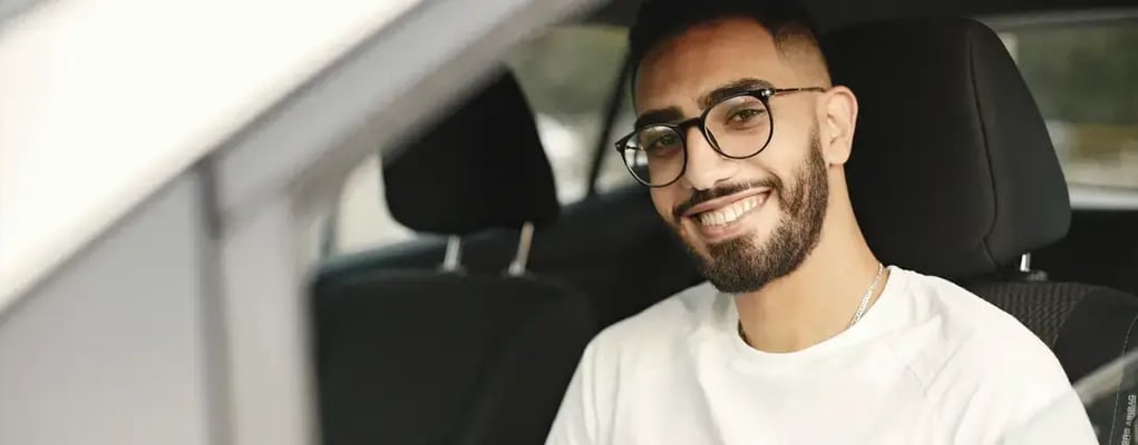 Homem de óculos dentro de carro sorrindo para câmera