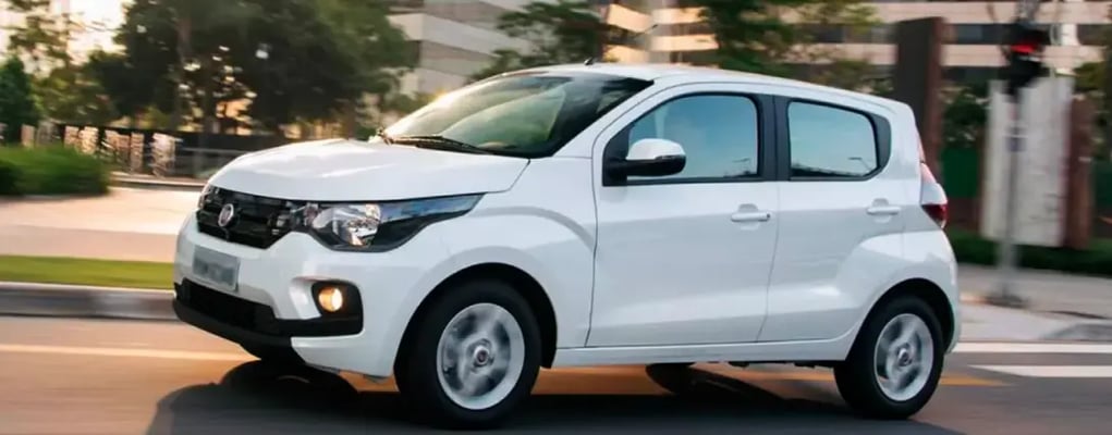 Visão lateral de um carro fiat mobi branco andando nas ruas de uma cidade