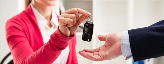 Mulher sorridente entregando a chave do carro na mão de um homem