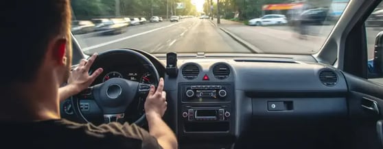 Homem com as mãos no volante dirigindo o carro em rua da cidade