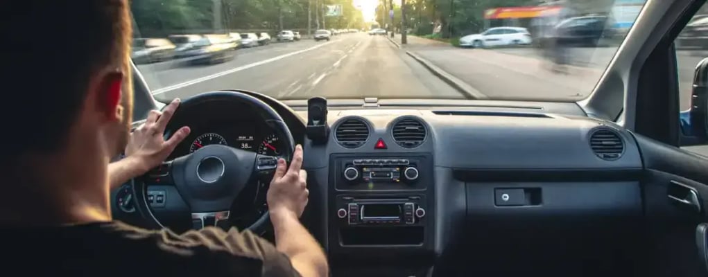 Homem com as mãos no volante dirigindo o carro em rua da cidade