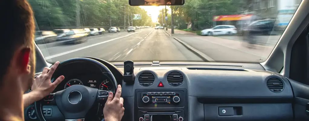 Motorista de app dirigindo em uma cidade movimentada, com um celular no painel mostrando o mapa