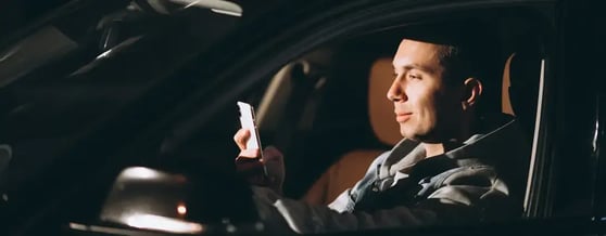 Motorista de aplicativo dentro do carro em um dia ensolarado olhando para o celular