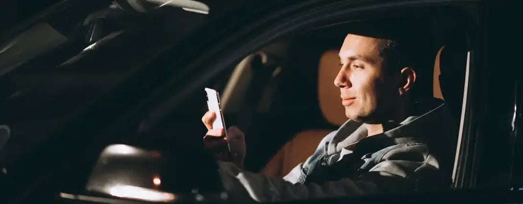 Motorista de aplicativo dentro do carro em um dia ensolarado olhando para o celular