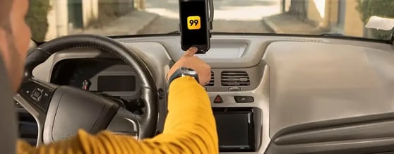 Motorista de aplicativo dentro do carro, iniciando o app da 99