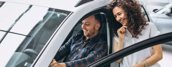 Homem dentro de carro segurando o volante com a porta aberta e mulher do lado de fora olhando para o carro