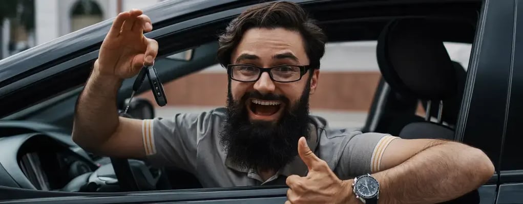 Homem sorridente fazendo sinal positivo e segurando a chave do carro por assinatura