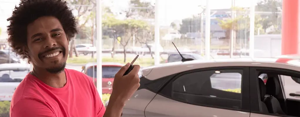 Homem sorridente segurando a chave de um carro na loja da Kovi