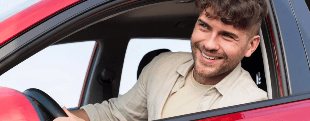 Motorista de aplicativo dentro de um carro vermelho, olhando pela janela