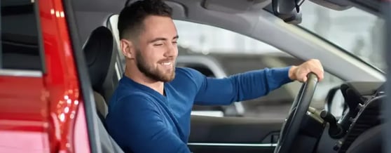 Homem sorrindo dentro do carro, com a mão no volante, alugual sem cartão de crédito