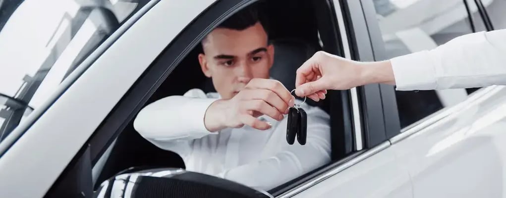 Homem de camisa branca dentro do carro recebendo as chaves do veículo da mão de vendedora