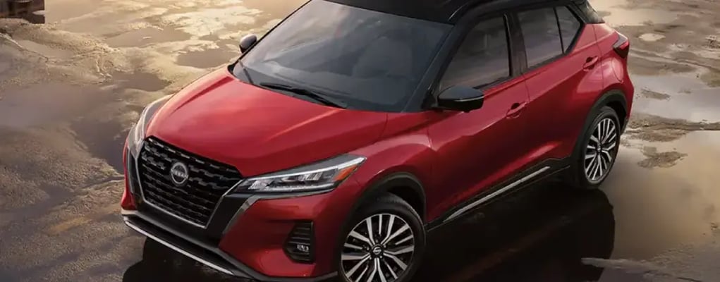 Nissan Kicks vermelho estacionado, refletindo o sol em poças d'água ao redor
