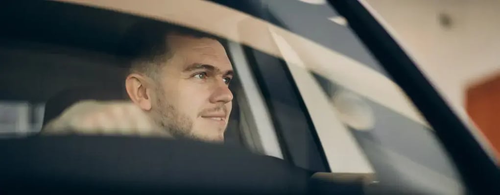 Homem dentro de carro segurando o volante e olhando pela janela