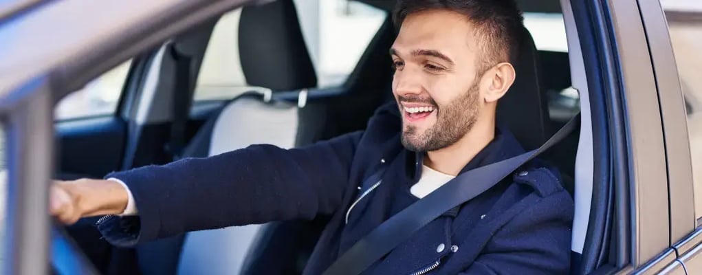 Homem sorridente segurando o volante dentro do carro