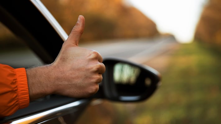 Mão com polegar para cima de dentro de um veículo andando na estrada