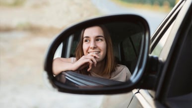 Mulher motorista de aplicativo sorrindo olhando pelo retrovisor do carro