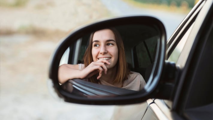 Mulher motorista de aplicativo sorrindo olhando pelo retrovisor do carro