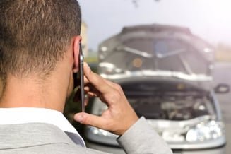 Homem fazendo ligação pelo celular em frente a um veículo com o capô aberto