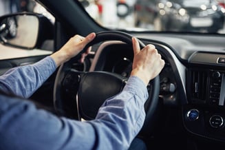 Close de duas mãos segurando o volante de um carro alugado