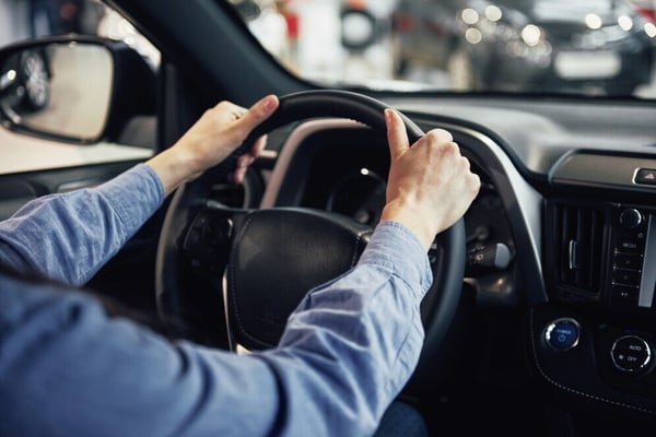 Close de duas mãos segurando o volante de um carro alugado