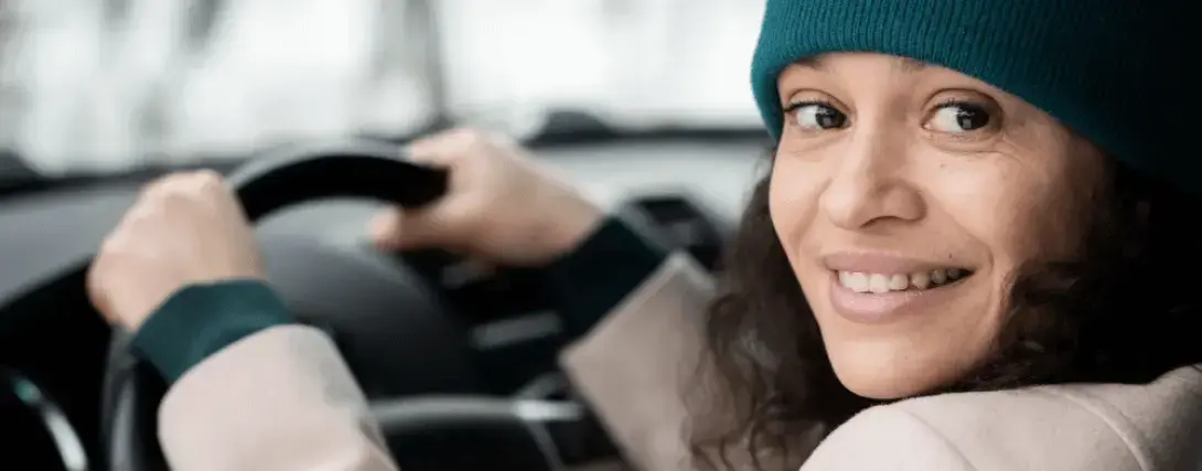 Mulher motorista vestindo uma touca de inverno segurando o volante e olhando para a câmera