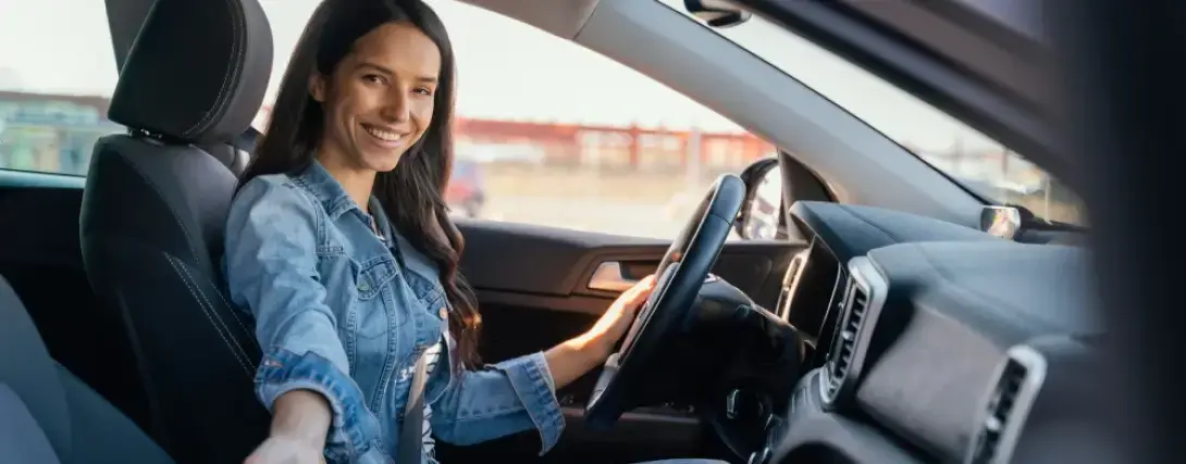 Mulher motorista de aplicativo sorridente segurando o volante e olhando para a câmera